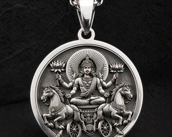 May include: Silver pendant necklace featuring a detailed depiction of a deity seated in a chariot pulled by two horses. The pendant has a circular design with intricate relief carvings and a chain.