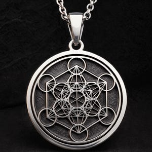 Peut inclure: Un collier pendentif argenté avec un pendentif circulaire orné d'un motif géométrique. Le pendentif présente un motif complexe de formes et de lignes interconnectées, sur un fond texturé. La chaîne est également argentée.