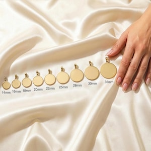 A hand is holding a row of gold-colored pendants, each with a different size, against a white fabric background.