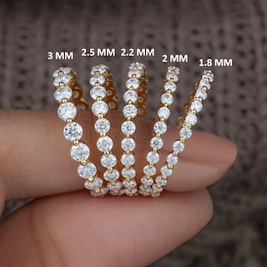 Könnte beinhalten: Fünf goldene Ewigkeitsringe mit runden Diamanten, die in der Größe von 1,8 mm bis 3 mm reichen. Die Ringe sind nach Größe geordnet, wobei der kleinste Ring rechts und der größte Ring links ist.