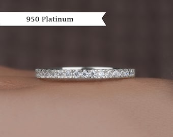 May include: A platinum ring with a band of small, clear gemstones. The ring is set against a blurred background. The text "950 Platinum" is displayed above the ring.