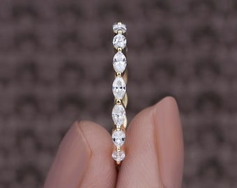 May include: A gold band ring featuring a series of marquise-cut, clear gemstones. The gemstones are set in a row along the ring's band. The ring is held against a brown background.