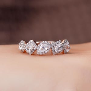 May include: A rose gold band ring featuring a series of five prominent clear stones in alternating pear and square shapes, each surrounded by a halo of small pavé diamonds. The text DiamondFineJewels is visible on the side of the ring band.