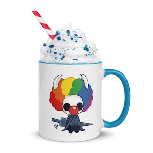 Può includere: Tazza in ceramica bianca con manico e bordo blu, con un design a fumetto di un clown con afro arcobaleno, naso rosso e un'arma. La tazza è sormontata da panna montata, zuccherini blu e una cannuccia a righe rosse e bianche.
