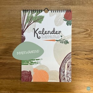 May include: A spiral-bound calendar featuring illustrations of seasonal fruits and vegetables. The word "Kalender" is displayed prominently, with additional text in German. A green oval sticker reads "IMMERW&Auml;HREND". The calendar includes images of beets, strawberries, and asparagus.