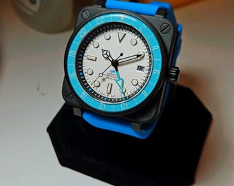 Könnte beinhalten: Eine schwarz-blaue Armbanduhr mit weißem Zifferblatt und blauer Lünette. Die Uhr hat ein Datumsfenster bei 3 Uhr und den Text "GMT Automatic Water Resistant 10BAR 100M" auf dem Zifferblatt.