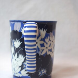 May include: A white ceramic mug with a black handle and the text "But First, Coffee" in a black, bold font. The mug is on a white surface.