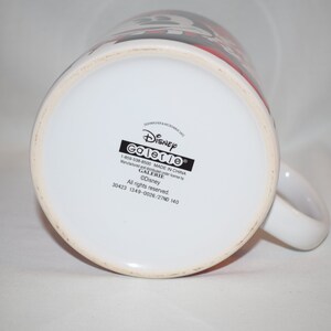 May include: White ceramic mug with a black and red Disney Galerie logo. The mug has a black handle and the text "Disney Galerie 1-800-538-4500 MADE IN CHINA Manufacturer for all items by GALERIE &copy;Disney All rights reserved. 30423 1349-0026/2710 140" printed on the bottom.