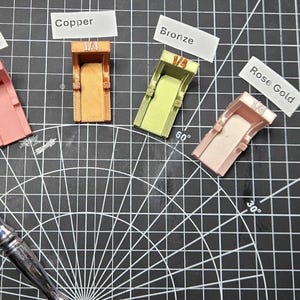 May include: Five 1/4 inch socket adapters in various colors including pink, copper, bronze, and rose gold, arranged in a fan shape. One adapter is attached to a silver metal ratchet handle. Labels identify the colors as Rainbow, Copper, Bronze, and Rose Gold.