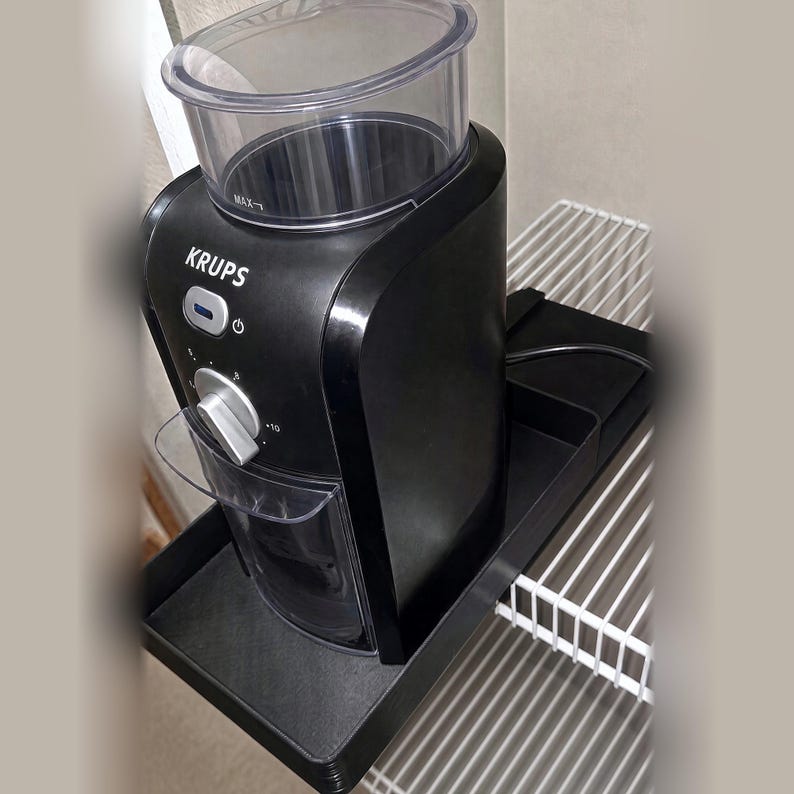 Pu&ograve; includere: Un macinacaff&egrave; Krups nero con una tramoggia in plastica trasparente sulla parte superiore, una manopola di controllo argentata e un pulsante di accensione. L'apparecchio presenta un contenitore di raccolta trasparente sul davanti e poggia su un vassoio nero.