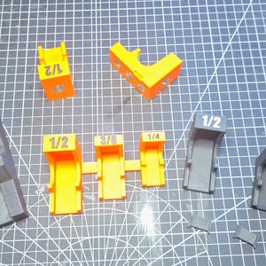 May include: A collection of 3D printed plastic corner clamping jigs in various sizes and colors, including black, orange, and purple. Each piece is clearly labeled with its specific size, such as 3/4, 1/2, 3/8, and 1/4, indicating the measurement for each tool.