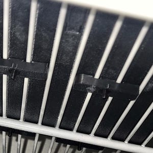 Pu&ograve; includere: Uno scaffale in filo metallico bianco con due clip in plastica nera fissate alle barre verticali. Le clip sono rettangolari con una piccola linguetta sporgente sulla parte anteriore, progettate per fissare la struttura in filo.