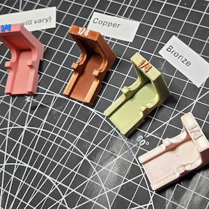 May include: Five L-shaped plastic corner brackets in various colors including pink, copper, bronze, and rose gold. Each bracket is labeled with 1/4 and is positioned next to a metal ratchet tool. Labels include Rainbow, Copper, Bronze, and Rose Gold.