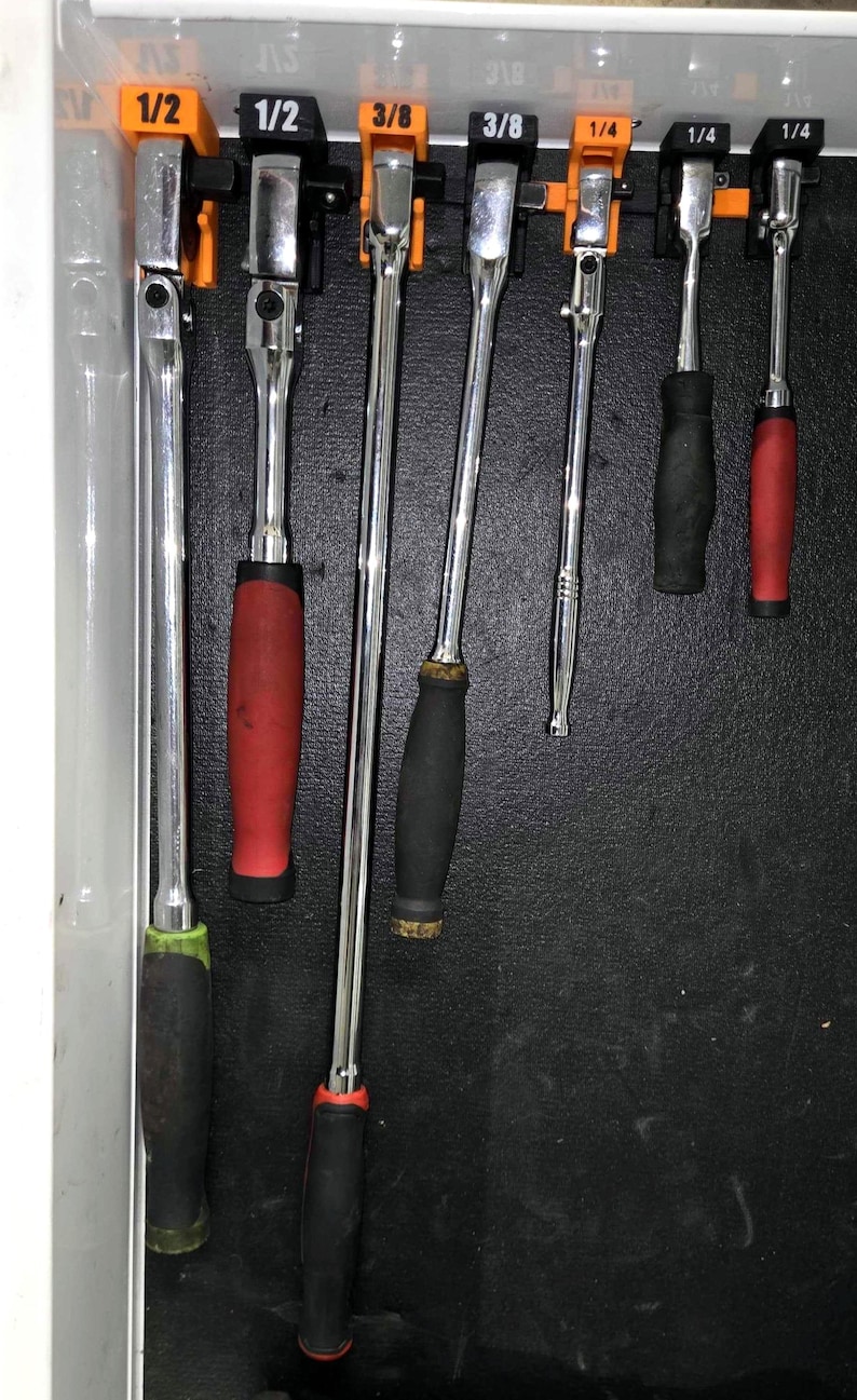 May include: A set of seven chrome-plated metal ratchets with various handle colors including black, red, and green, organized on orange and black plastic holders labeled 1/2, 3/8, and 1/4, mounted vertically inside a tool drawer.