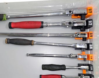 Può includere: Una collezione di cricchetti in metallo cromato con impugnature di vari colori, tra cui rosso e nero, organizzati in un cassetto su supporti in plastica arancione e nera etichettati 1/2, 3/8 e 1/4 per indicare le dimensioni dell'attacco.
