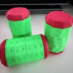 May include: Three green and red puzzle cylinders with numbered segments. One cylinder is horizontal, while two stand upright. The numbers are in white, and the cylinders are made of plastic.