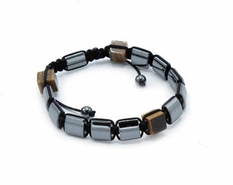 Puede incluir: Un brazalete negro con cuentas de color plateado y marrón cuadradas. El brazalete tiene un cierre de nudo deslizante.
