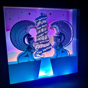 May include: A papercraft light-up sculpture of two winged figures with the text "We don't know how much longer we can withstand the nothing" on a tower in the centre.