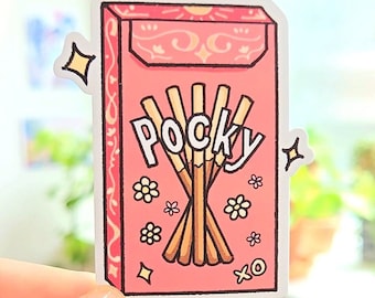 Puede incluir: Una pegatina rosa y blanca con una ilustración de dibujos animados de una caja de palitos Pocky. La caja tiene un diseño floral y el texto "Pocky" está escrito en letras blancas. Hay pequeñas flores blancas y estrellas alrededor de la caja.