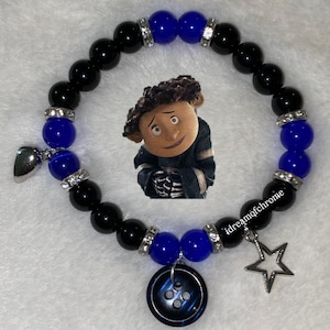 K&ouml;nnte beinhalten: Ein Armband mit schwarzen und blauen Perlen, mit Strass-Abstandshaltern. Es hat Charms, darunter ein Stern, ein Knopf und ein silbernes Herz. Ein Cartoon-Bild ist ebenfalls enthalten. Der Text "idreamofchrome" ist sichtbar.