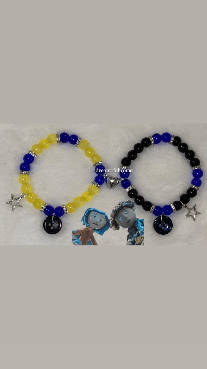 K&ouml;nnte beinhalten: Zwei Armb&auml;nder mit Perlen. Eines ist gelb und blau, das andere schwarz und blau. Jedes Armband hat einen Knopf, einen Stern und einen Herzanh&auml;nger. Die Armb&auml;nder sind vom Film "Coraline" inspiriert.