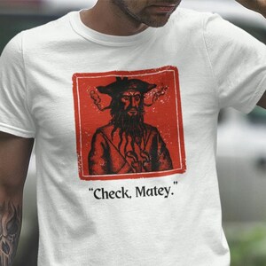 May include: White t-shirt with a red square graphic of a pirate with a beard and a bandana. The text "Check, Matey." is printed below the graphic.