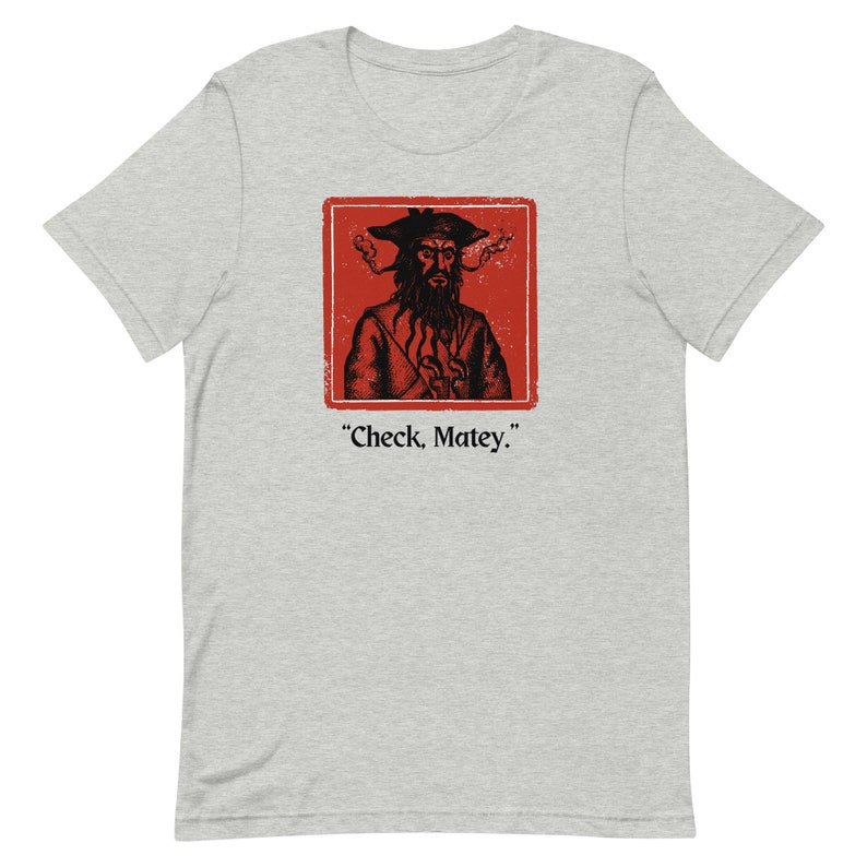 May include: A gray t-shirt with a red square featuring a black and white illustration of a pirate with a beard and a hat. The text "Check, Matey." is below the square.