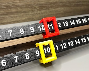 May include: Two black measuring rulers with white numerals and red and yellow markers. The rulers are marked with numbers from 6 to 16. The red marker is on the number 11, and the yellow marker is on the number 10. The rulers are made of plastic.