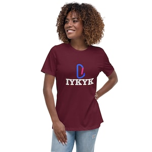 May include: A maroon t-shirt with a graphic design. The design features a blue and pink shape above the white text "IYKYK". The shirt has short sleeves and a relaxed fit.