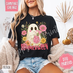 May include: Black t-shirt with a graphic of a ghost drinking a pink beverage, surrounded by flowers. The word "SUMMERWEEN" is printed in pink. The shirt is labeled "Comfort Colors" and "DTG Printed".