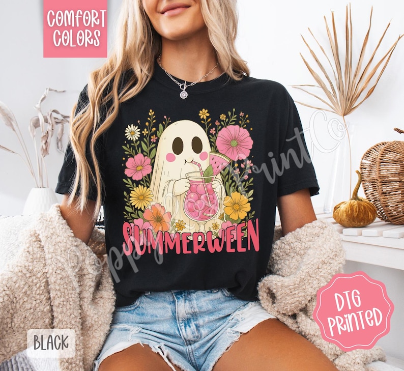 May include: Black t-shirt with a graphic of a ghost drinking a pink beverage, surrounded by flowers. The word "SUMMERWEEN" is printed in pink. The shirt is labeled "Comfort Colors" and "DTG Printed".