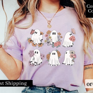 May include: A purple t-shirt with a graphic of six ghosts holding flowers. The ghosts are white and the flowers are pink, orange, and yellow. The text "Comfort Colors" is in the upper right corner of the image. The text "orchid" is in the lower right corner of the image. The text "Fast Shipping" is in the lower left corner of the image.