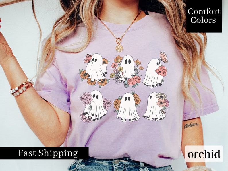 May include: A purple t-shirt with a graphic of six ghosts holding flowers. The ghosts are white and the flowers are pink, orange, and yellow. The text "Comfort Colors" is in the upper right corner of the image. The text "orchid" is in the lower right corner of the image. The text "Fast Shipping" is in the lower left corner of the image.