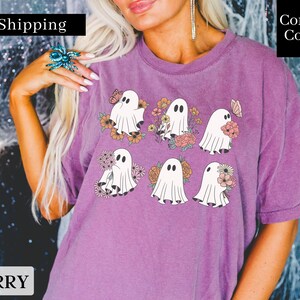 May include: Purple t-shirt with a graphic of six white ghosts holding flowers. The ghosts are surrounded by pink, orange, and yellow flowers. The shirt has the text "Fast Shipping" and "Comfort Colors" on it.