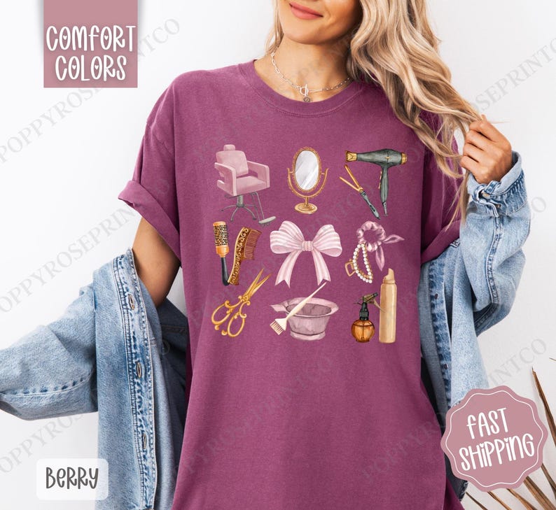 May include: A purple t-shirt with a graphic design of various hair salon tools, including a hair dryer, scissors, a hairbrush, a bowl, a spray bottle, a hair tie, a pearl necklace, a pink bow, and a salon chair.