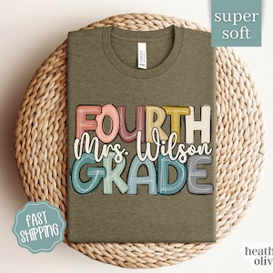 May include: A heather olive green t-shirt with the text "FOURTH Mrs. Wilson GRADE" in colorful, hand-drawn lettering.