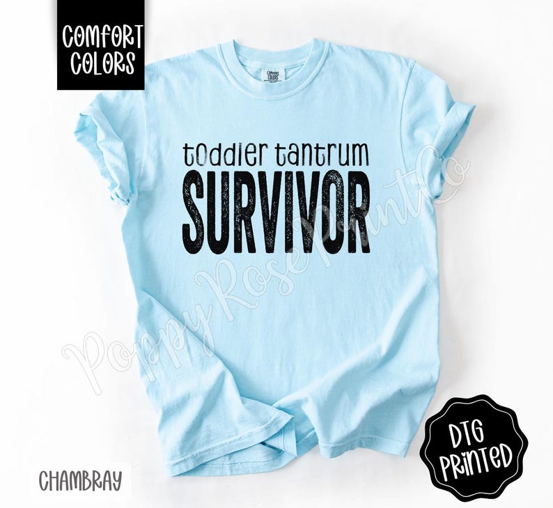 May include: Light blue t-shirt with the words "toddler tantrum SURVIVOR" in black lettering. The shirt has short sleeves and a crew neck. The words "Comfort Colors" and "Chambray" are also visible.