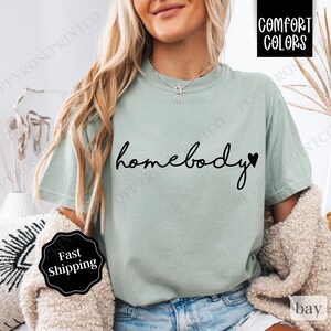 May include: A light green t-shirt with the text "homebody" in black cursive lettering and a small black heart.