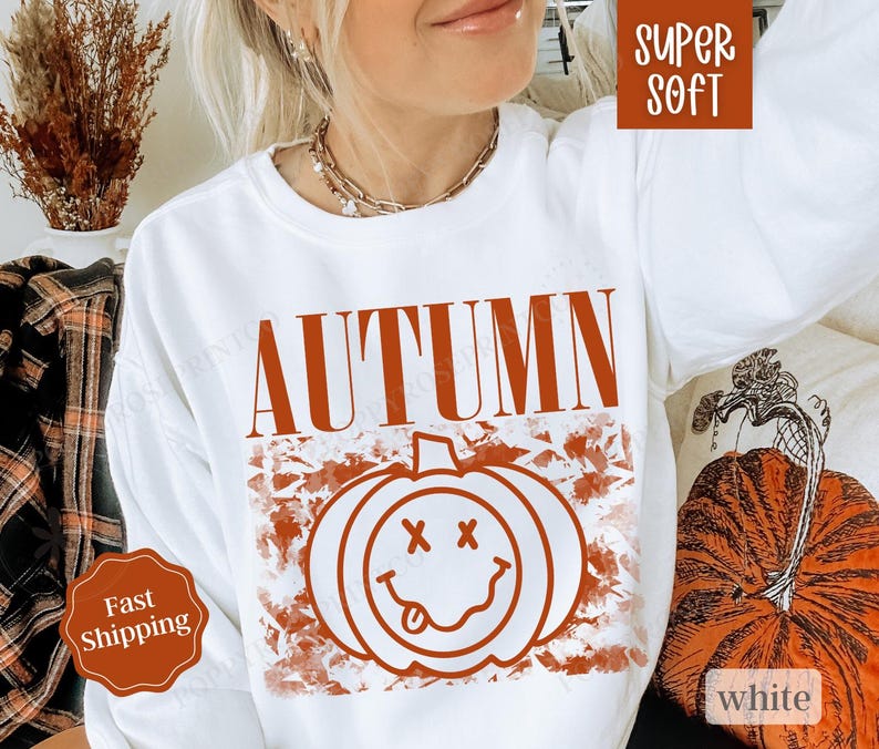 May include: White sweatshirt with the word "AUTUMN" in orange text and a smiling pumpkin graphic with a red outline. The pumpkin has a red tongue sticking out and two red X's for eyes.