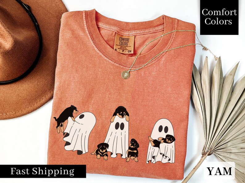 May include: A peach-colored t-shirt with a graphic of four black and brown puppies dressed as ghosts. The text "Comfort Colors" is printed on the tag.