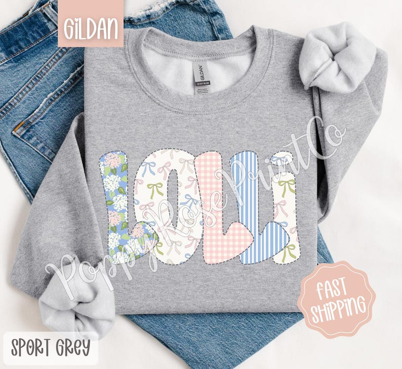 May include: A gray sweatshirt with the name "Lolli" spelled out in colorful patchwork letters. The letters are made of different fabrics with floral, gingham, and bow patterns.