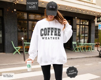 May include: White sweatshirt with the text "COFFEE WEATHER" in black lettering. The sweatshirt is being worn by a person holding a white coffee cup.