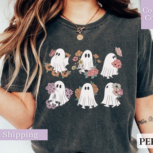 May include: A dark gray t-shirt with a graphic of six white ghosts holding flowers. The flowers are pink, orange, and yellow. The text "Comfort Colors" is in the upper right corner of the image.