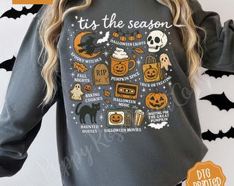May include: Dark gray sweatshirt with a Halloween-themed graphic. The design includes a crescent moon, witch, pumpkin spice mug, skull, and the phrase "'tis the season." Additional elements include ghosts, bats, and pumpkins.