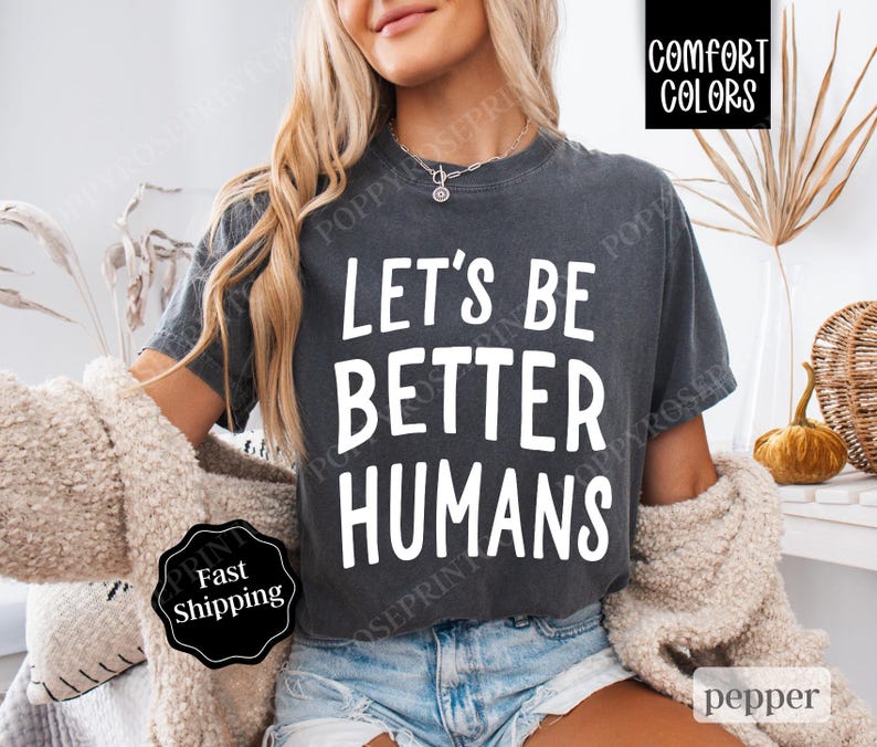 May include: A dark gray cropped t-shirt with the text "Let's Be Better Humans" printed in white. The shirt is being worn by a person.