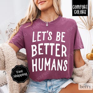 May include: A mauve colored t-shirt with the text "Let's Be Better Humans" printed in white.