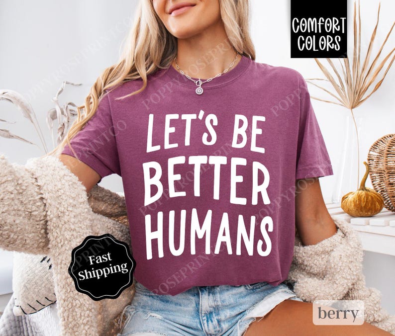 May include: A mauve colored t-shirt with the text "Let's Be Better Humans" printed in white.