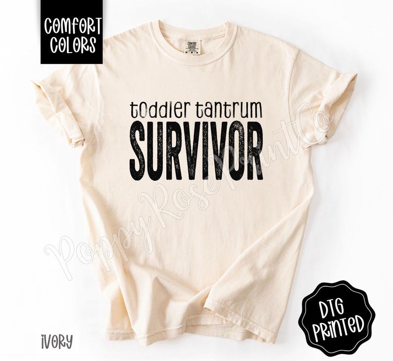 May include: Ivory-colored t-shirt with the words "toddler tantrum SURVIVOR" in black, distressed font. The shirt has rolled-up sleeves and is labeled "Comfort Colors" and "DTG Printed".