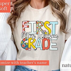 May include: A beige t-shirt with the text "FIRST Mrs. Wilson GRADE" in colourful letters with a variety of patterns. The text is customisable with a teacher's name.