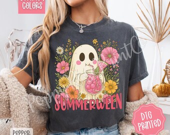 May include: Dark gray t-shirt featuring a cartoon ghost enjoying a pink drink with a watermelon slice, surrounded by flowers. The word "SUMMERWEEN" is printed in pink. The shirt has "COMFORT COLORS" and "DTG PRINTED" labels.